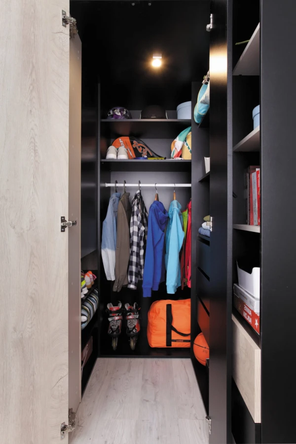 Moderner begehbarer Kleiderschrank in Schwarz und Eiche mit Beleuchtung und Sportequipment.