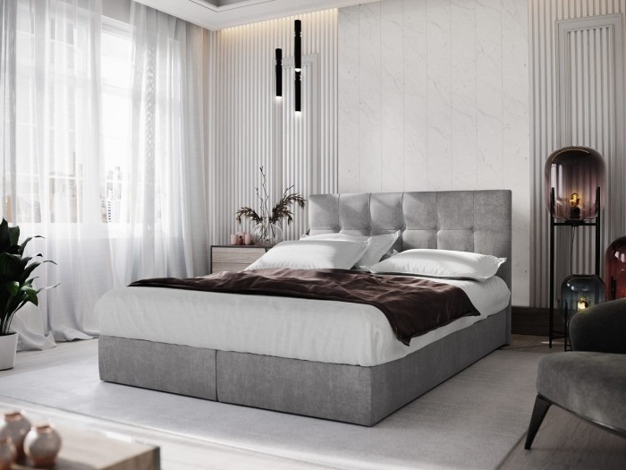 Hellgraues Boxspringbett mit elegantem Kopfteil und weißer Bettwäsche.