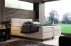 Cremefarbenes Boxspringbett in modernem Schlafzimmer mit Blick ins Grüne und Holzverkleidung.