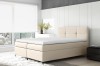 Elegantes beiges Boxspringbett in modernem Schlafzimmer mit weißer Matratzenauflage.