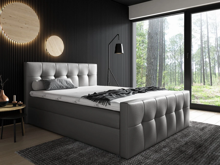 Modernes Boxspringbett in Hellgrau mit Quadratsteppung in dunklem Schlafzimmer mit Waldblick.