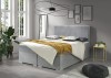Hellgraues Boxspringbett in einem modernen Schlafzimmer mit großen Fenstern.