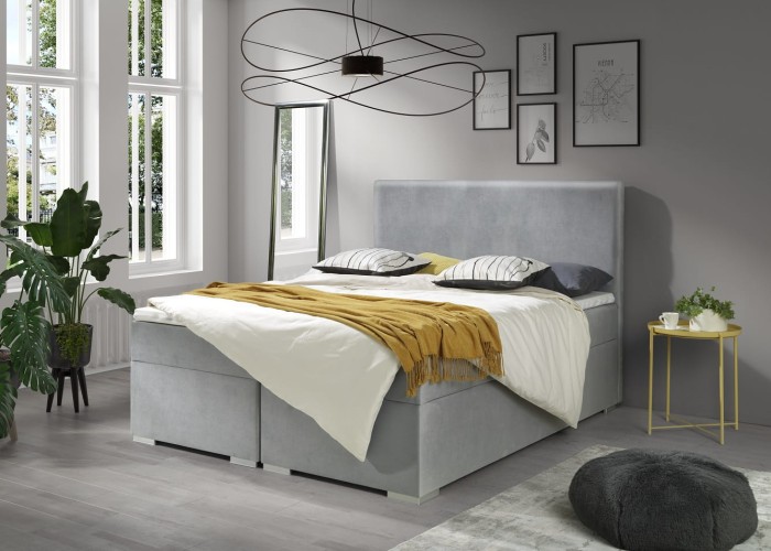 Hellgraues Boxspringbett in einem modernen Schlafzimmer mit großen Fenstern.