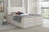 Elegantes weißes Boxspringbett mit weichem Stoffbezug vor einer hellen Backsteinwand im Schlafzimmer.