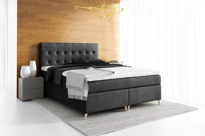 Dunkelgraues Boxspringbett mit Samtbezug und dekorativ gestepptem Kopfteil.