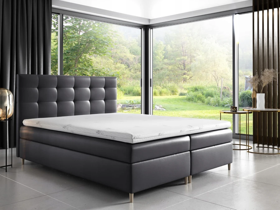 Anthrazitfarbenes Boxspringbett mit gestepptem Kopfteil in modernem Schlafzimmer mit Gartenblick.