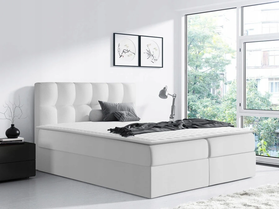 Elegantes weißes Boxspringbett mit hohem Kopfteil in modernem, lichtdurchflutetem Raum.