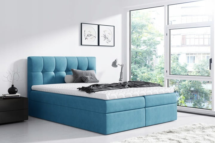 Blaues Boxspringbett mit gestepptem Kopfteil und gemütlichem Topper in hellem Schlafzimmer.