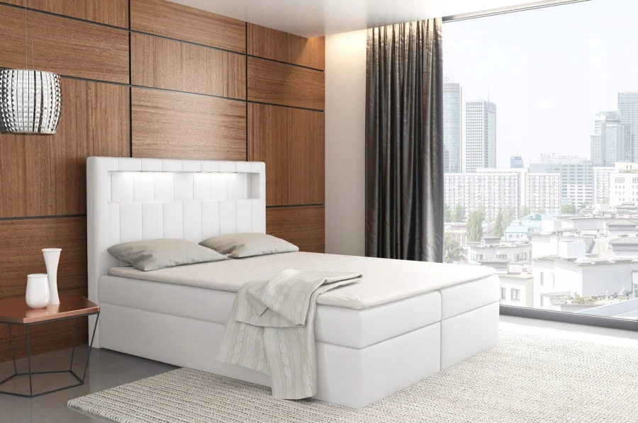 Weißes Boxspringbett mit LED-Kopfteil in einem hellen, modernen Schlafzimmer mit Blick auf die Stadt.