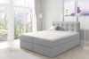 Hellgraues Boxspringbett mit gestepptem Kopfteil in lichtdurchflutetem Schlafzimmer.