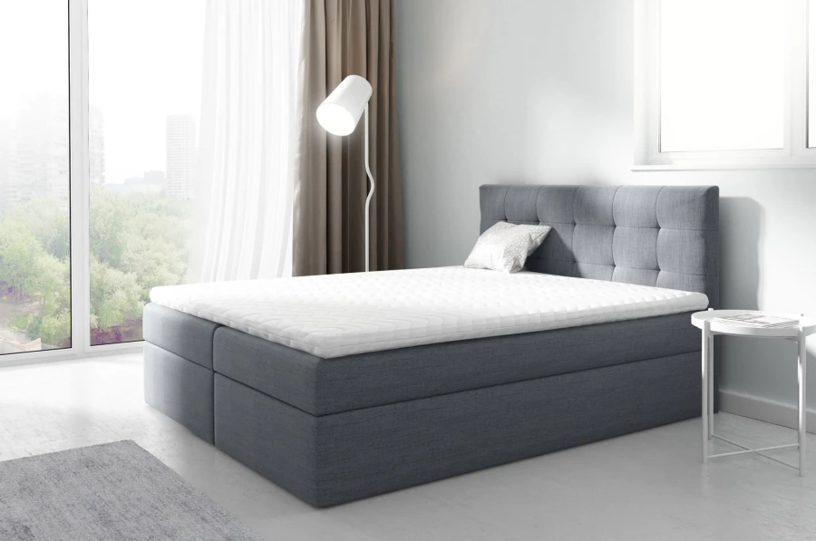 Graues Boxspringbett mit gestepptem Kopfteil in modernem Schlafzimmer mit Stadtblick.