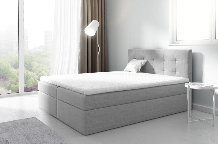 Hellgraues Boxspringbett mit hohem gepolstertem Kopfteil und komfortabler Matratze.