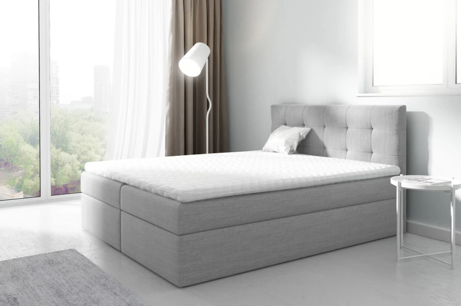 Hellgraues Boxspringbett mit hohem gepolstertem Kopfteil und komfortabler Matratze.