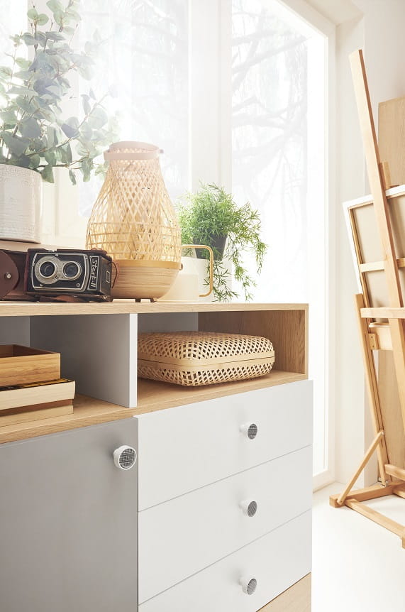 Modernes Sideboard mit dekorativer Kamera und geflochtener Laterne in lichtdurchflutetem Atelier.