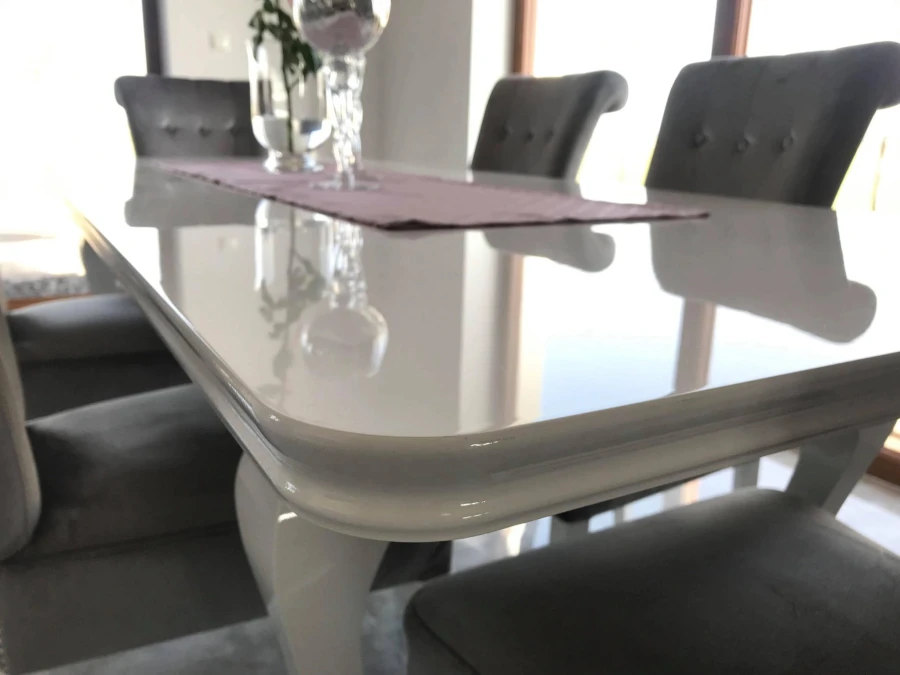 Nahaufnahme einer weißen Hochglanz-Tischplatte mit abgerundeter Kante und Reflexionen.