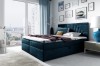 Dunkelblaues Boxspringbett mit Stauraum und gestepptem Kopfteil in hellem Zimmer.