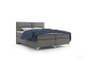 Modernes Boxspringbett in Grau mit blauer Decke auf weißem Hintergrund.