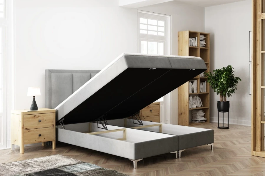 Graues Polsterbett im Schlafzimmer mit geöffnetem Bettkasten für viel Stauraum.