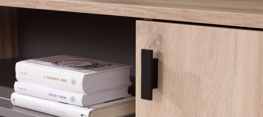 Schwarzer Griff an heller Holzfront mit Bücherregal-Detail.