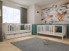 Weißes Massivholz-Kinderbett mit Rausfallschutz und Schubladen in einem gemütlichen Kinderzimmer.