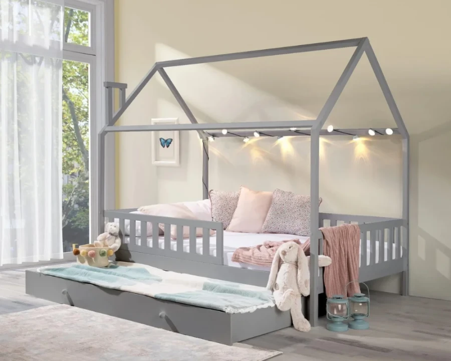 Gemütliches graues Hausbett mit Lichterkette und rosa Dekoration im hellen Kinderzimmer.
