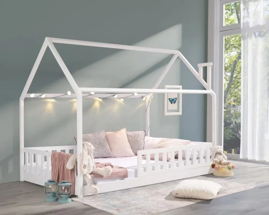 Weißes Kinderhausbett mit Rausfallschutz und Lichterkette in gemütlicher Atmosphäre.
