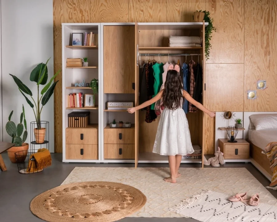 Mädchen im weißen Kleid vor einem geöffneten Kleiderschrank im modern eingerichteten Kinderzimmer.