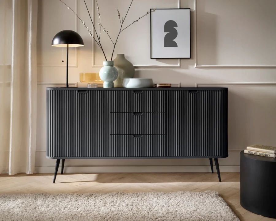 Schwarzes Sideboard im Wohnzimmer-Ambiente mit Lampe, Vasen und moderner Wandkunst dekoriert.