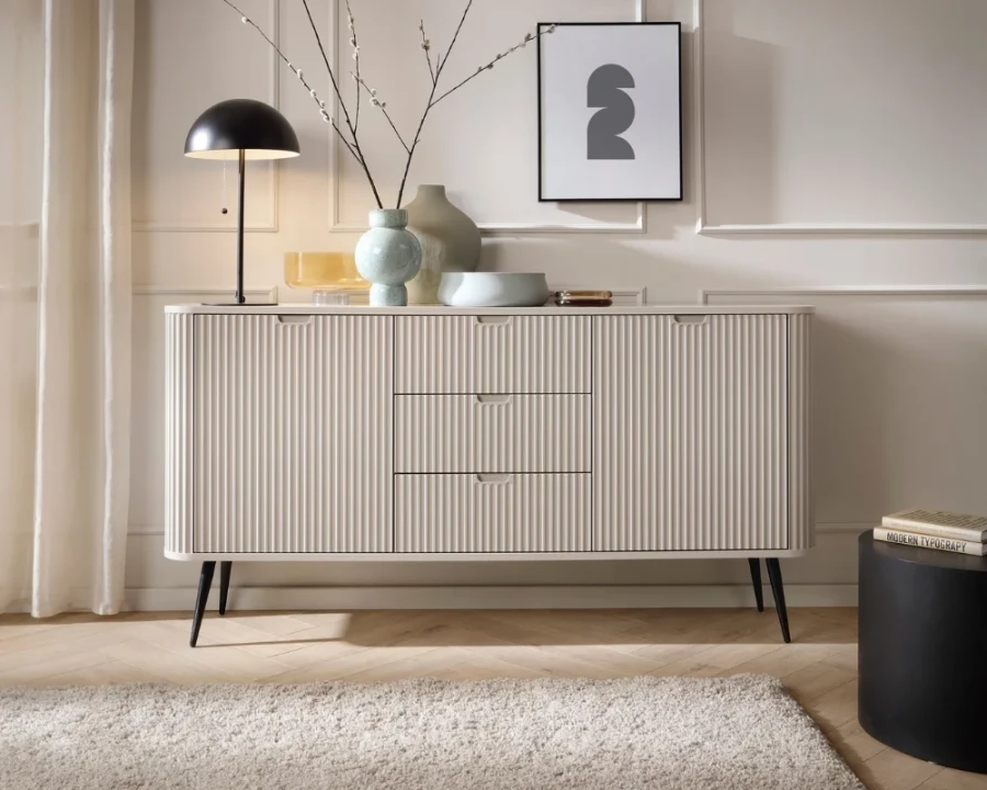Stilvoll dekoriertes Sideboard in Beige mit vertikalen Rillen und schwarzer Tischlampe.