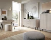 Modernes Wohnzimmer mit weißen Rillenmöbeln: Schreibtisch, Sideboard und Schrank in hellem Ambiente.