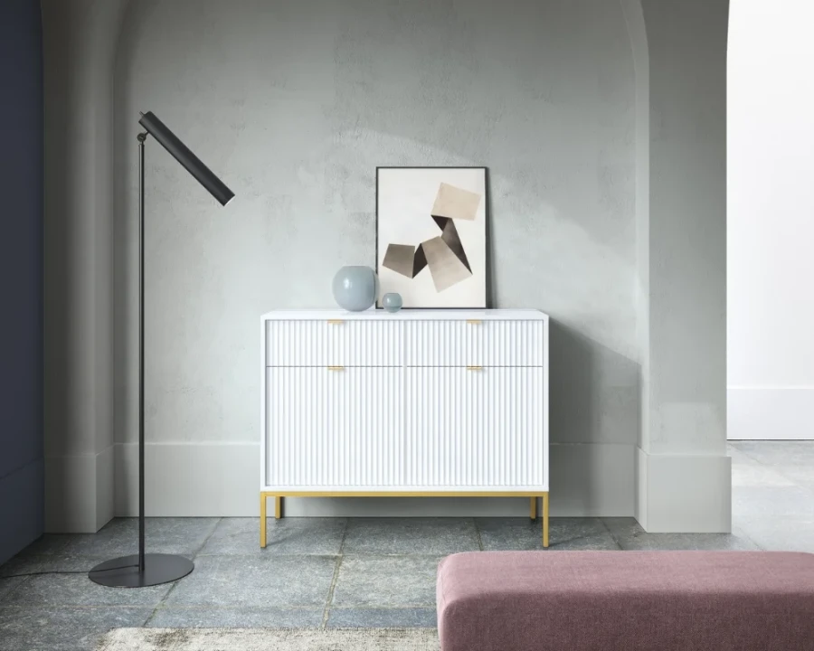 Stylische weiße Kommode mit Rillenoptik und goldenen Beinen in modernem Ambiente.
