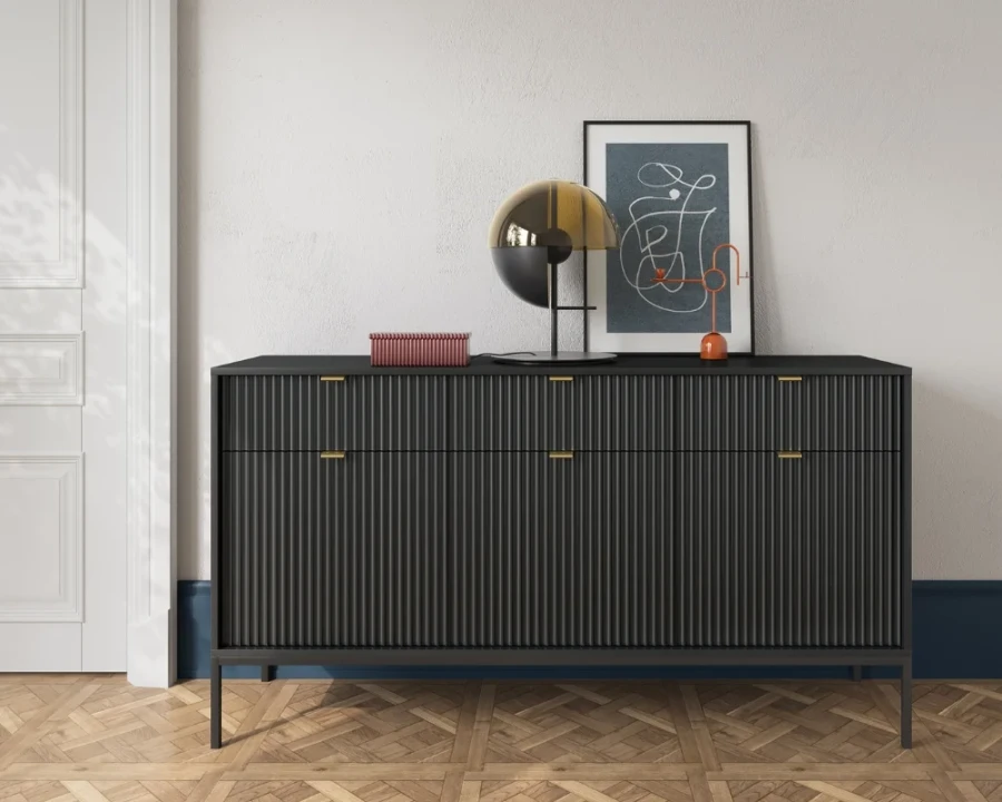 Schwarze Kommode mit Rillenstruktur und schwarzen Beinen vor einer weißen Wand.