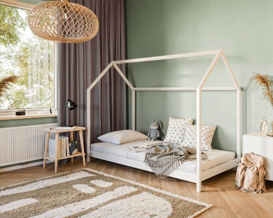 Weißes Kinder-Hausbett aus Holz in einem hellen, modern eingerichteten Kinderzimmer mit Dekoration.