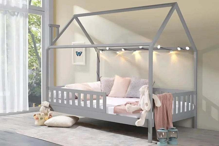 Dekoriertes graues Hausbett mit rosa Kissen, Kuscheltier und Lichterkette im hellen Kinderzimmer.