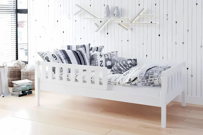 Modern white children's bed in Scandinavian style with guardrail and decorative cushions.