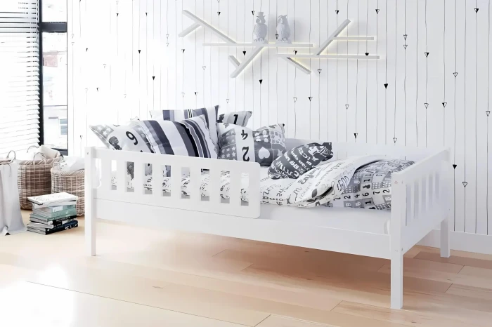 Modern eingerichtetes Kinderzimmer mit weißem Juniorbett und Kissen.