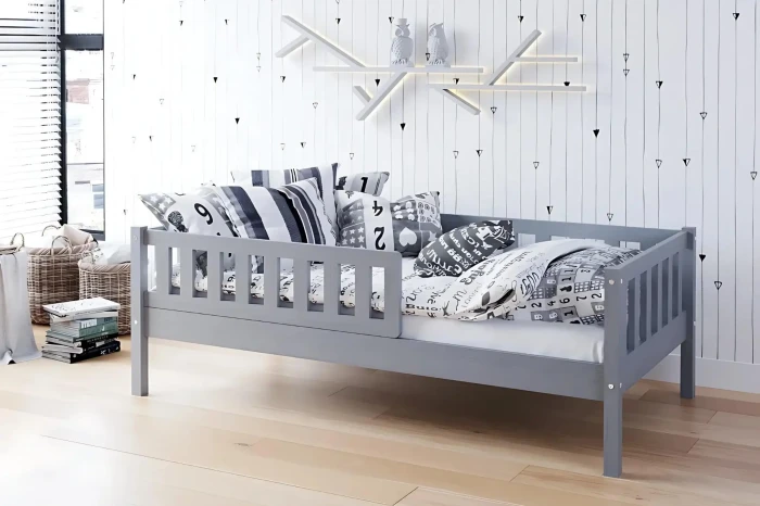 Graues Kinderbett mit Rausfallschutz und modernen Kissen in einem stilvollen Kinderzimmer.