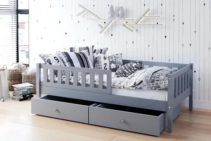 Graues Kinderbett mit Rausfallschutz und zwei Schubladen, dekoriert im modernen Kinderzimmer.