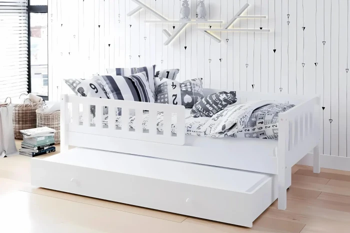 Weißes Kinderbett mit Ausziehfunktion und Kissen-Dekoration in hell eingerichteter Umgebung.
