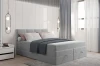 Gemütlich hergerichtetes hellgraues Boxspringbett mit weißen Kissen und dunkelgrauer Tagesdecke.