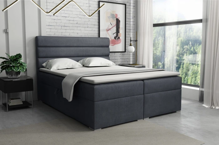 Dark grey box spring bed in a modernly furnished bedroom with a window front.