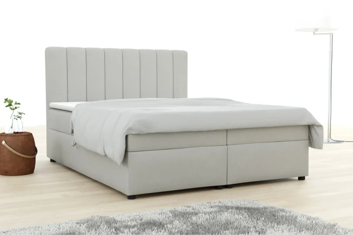 Elegantes Boxspringbett in Hellgrau mit hohem, gestepptem Kopfteil für ein modernes Schlafzimmer.