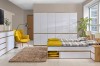 Helles Schlafzimmer-Ambiente mit weißem Kleiderschrank, Doppelbett und gelbem Sessel.