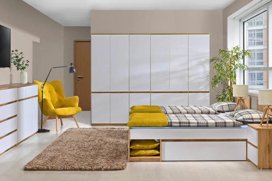 Modernes Schlafzimmer mit großem weißem Kleiderschrank, gelbem Sessel und weißem Stauraumbett.