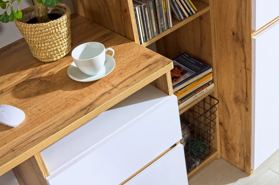 Detailansicht eines Schreibtisches mit Kaffeetasse, weißen Fronten und Holzmaserung.