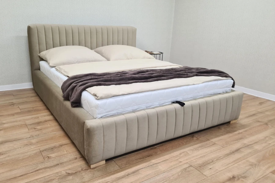 Modernes beige Polsterbett mit vertikal gestepptem Kopfteil in einem hellen Schlafzimmer.