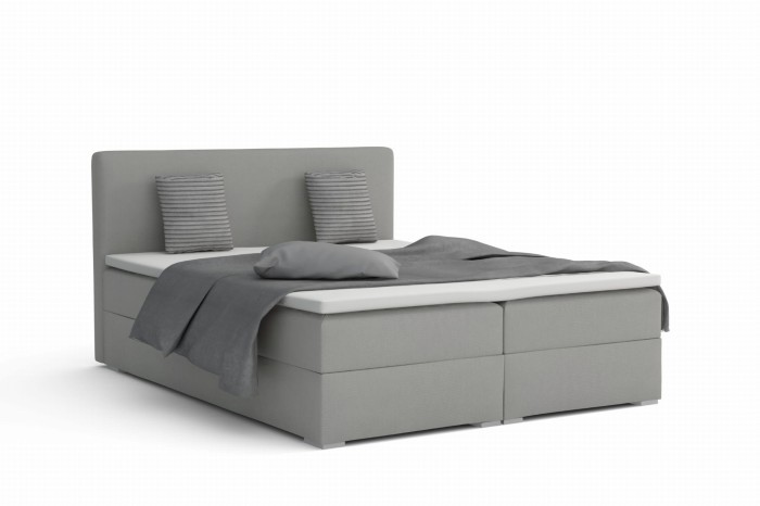 Hellgraues Boxspringbett mit grauer Tagesdecke vor weißem Hintergrund.