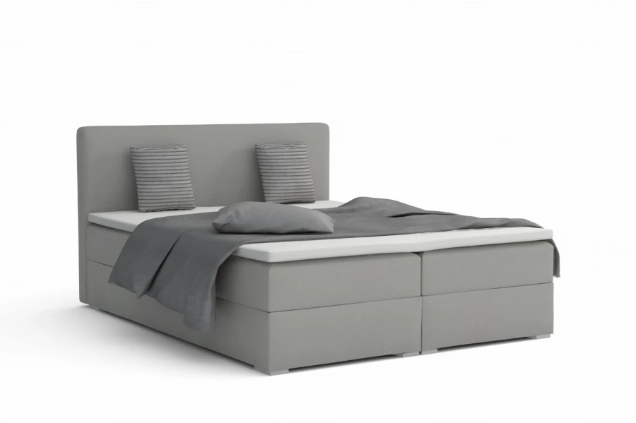 Lichtgrijs boxspringbed met grijze sprei tegen een witte achtergrond.