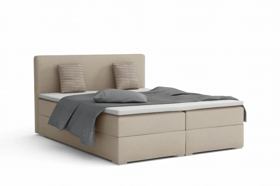 Sand-coloured boxspring bed with grey bed linen and decorative cushions.