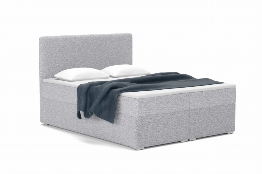 Graues Bouclé-Boxspringbett mit weißen Kissen und dunkelblauer Decke vor weißem Hintergrund.